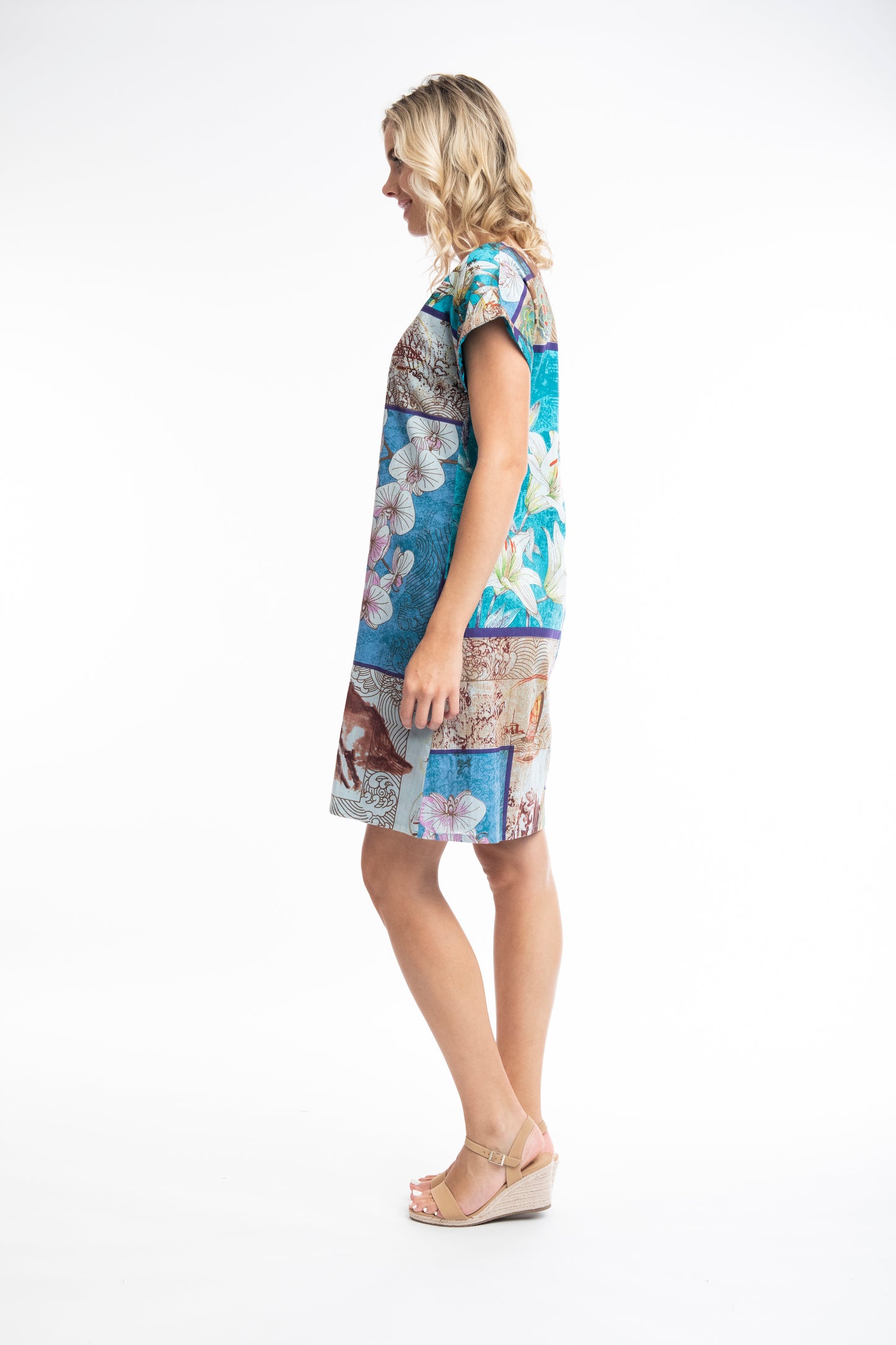 Woman posing in a colorful printed Orientique Leonardo Dress Shift Short Sleeve Reversible with hand raised, smiling against a white background.