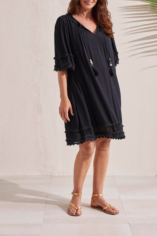 Woman modeling a black casual Tribal lined flowy dress with tassel trim details and gold sandals.