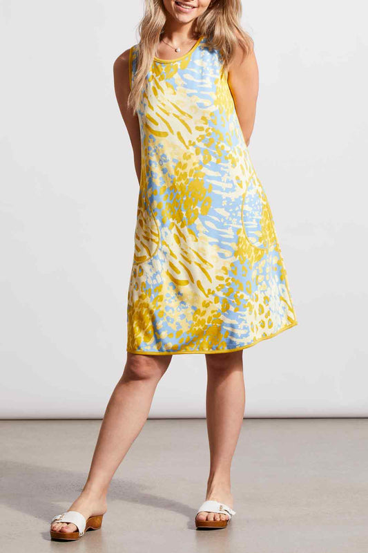 Woman wearing a versatile, sleeveless yellow and blue patterned Tribal Reversible A-Line Dress and white sandals.