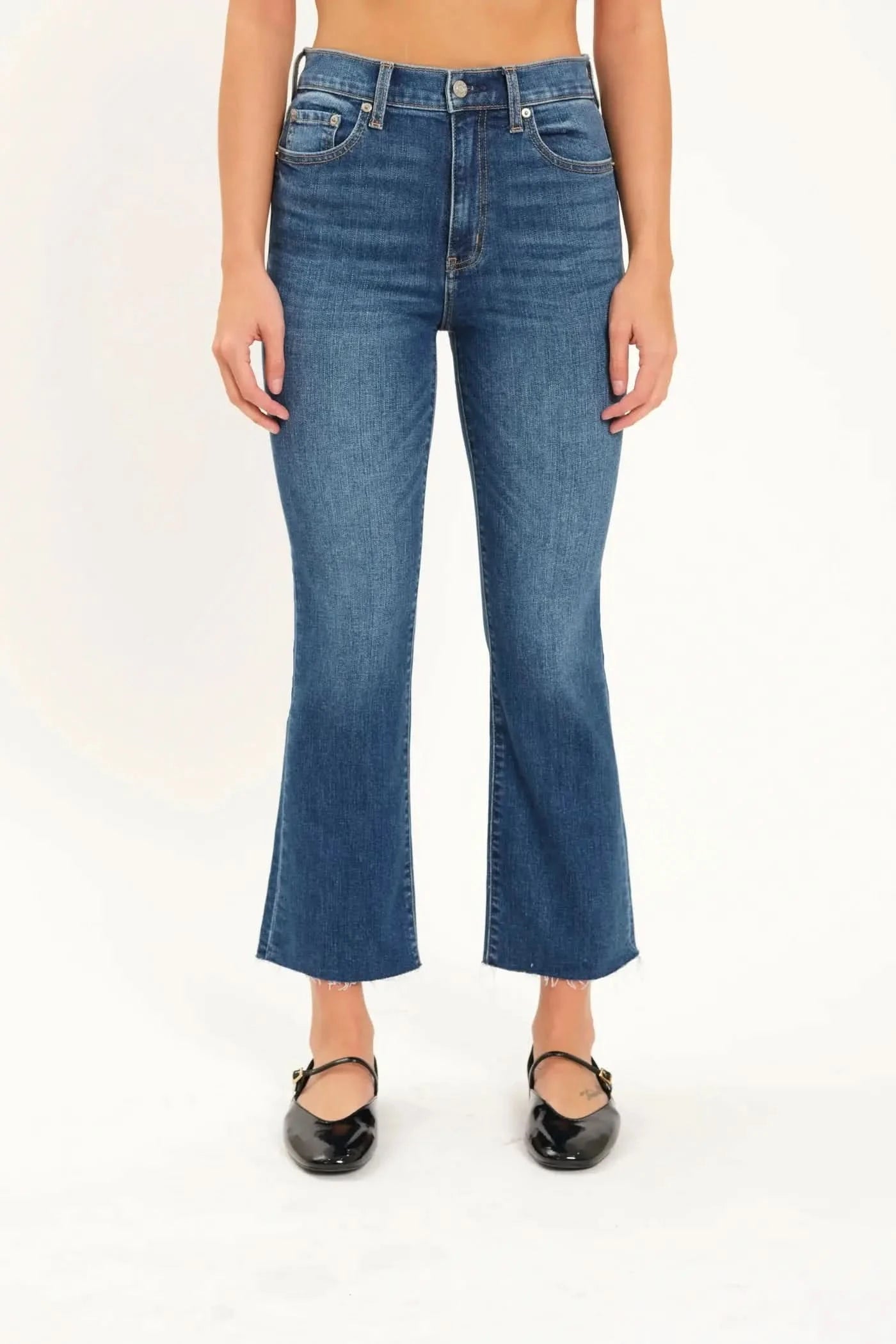 A person wearing Daze's Shy Girl High Rise Crop Flare jeans in denim blue and black ballet flats is standing against a plain white background.