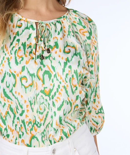 A person wearing an Esqualo Pastel Blouse and white pants stands against a white background, gently touching their hair.