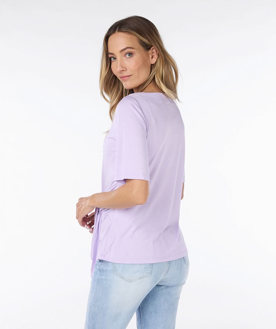 Woman wearing a cute and comfortable Lilac Top by Esqualo with a tie-front detail, paired with light blue jeans made from high-quality materials, posing against a plain white background.