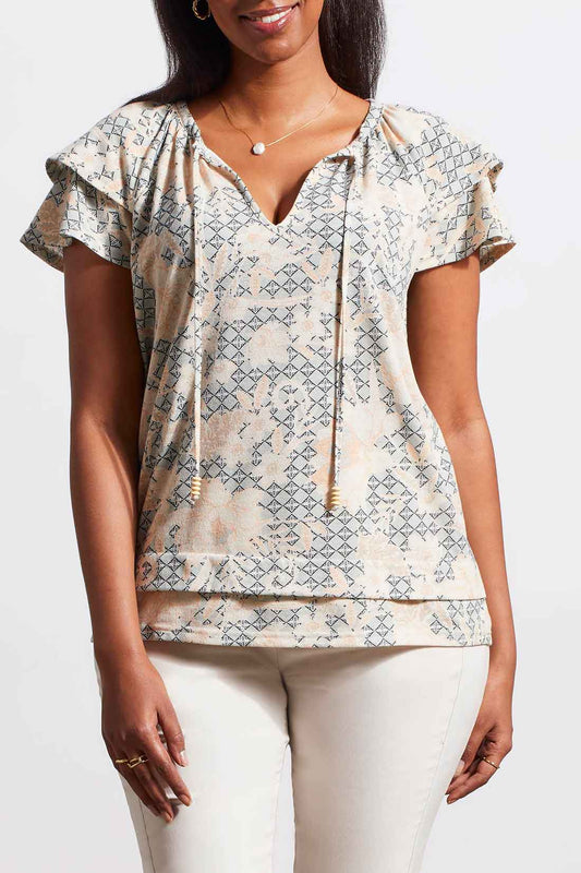 A woman wearing a stylish Tribal Short Sleeve Peasant Top with ruffled sleeves and white cotton pants.