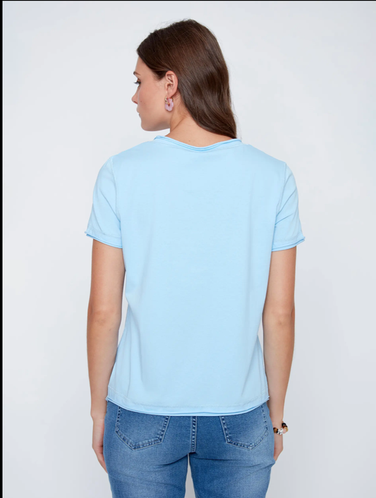 A woman models the CoCo Y Club T-shirt V-neck in light blue with blue jeans against a plain white background, highlighting this essential piece.