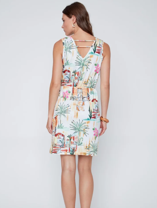 A woman models the CoCo Y Club Mini Palm Dress, a sleeveless, knee-length dress with a vibrant tropical print, set against a plain light gray background.