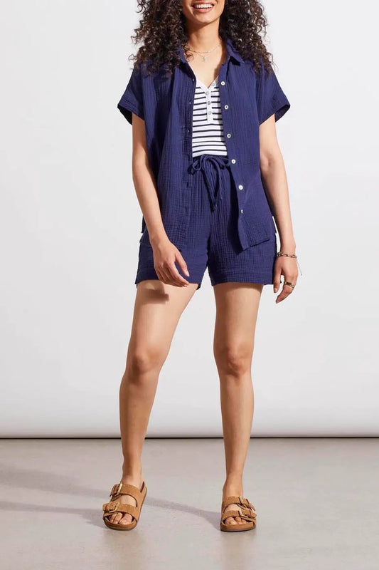 Woman in a casual blue romper with Tribal elastic waistband shorts, wearing a striped undershirt and brown sandals, poses for a fashion display.