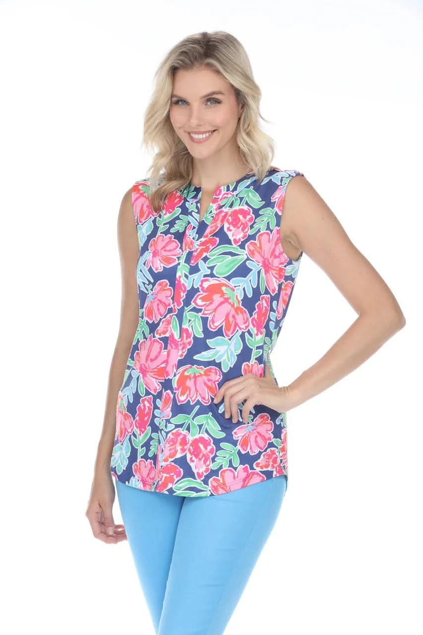 A person stands confidently against a white backdrop, smiling with one hand on their hip, wearing the feminine Rose Sleeveless Floral Top by Tango Mango made from wrinkle-resistant fabric, paired with stylish blue pants.