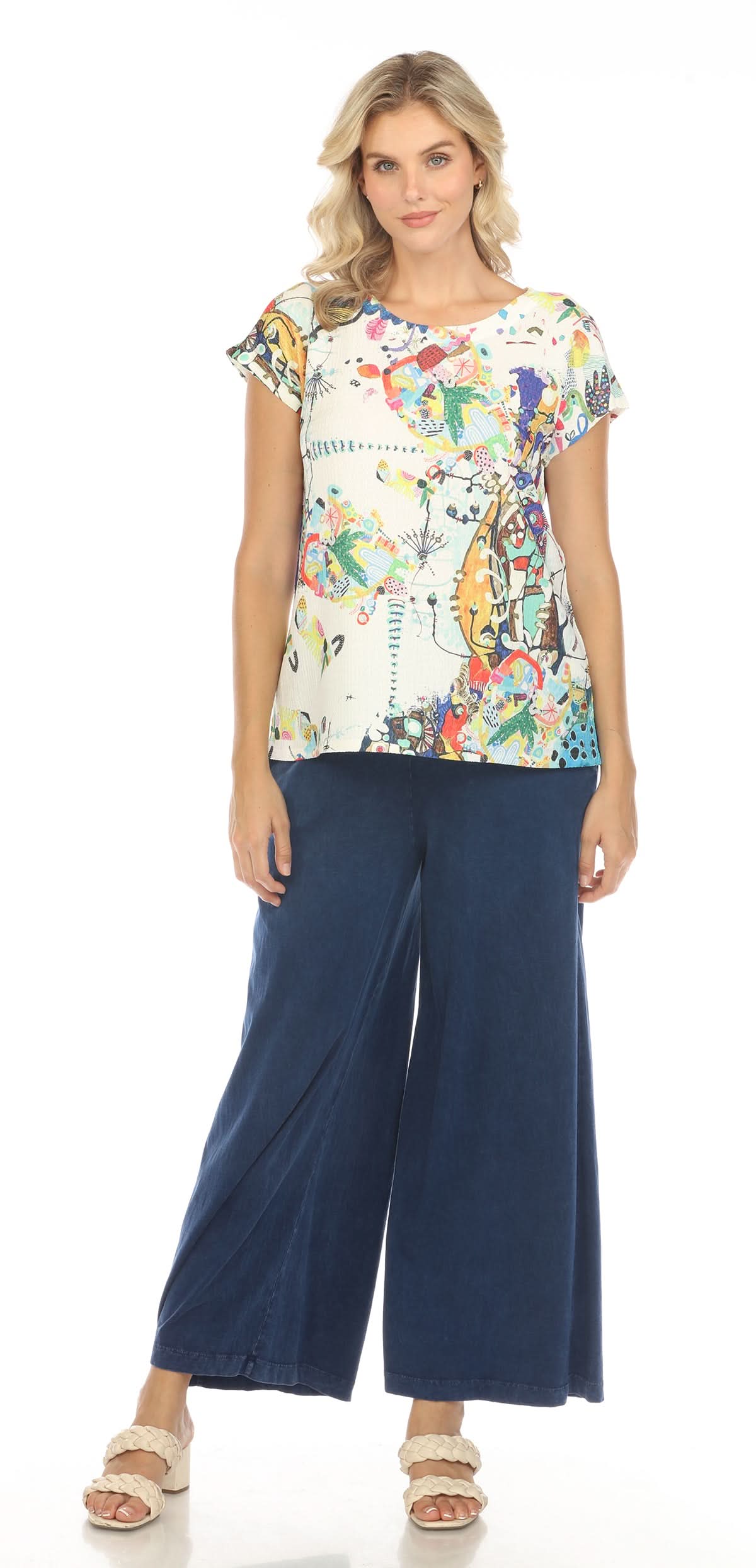 A woman with blonde hair, seen from the back, wears an Inoah Short Sleeve Crew Neck Top featuring a colorful abstract pattern and dark blue pants, standing against a white background.