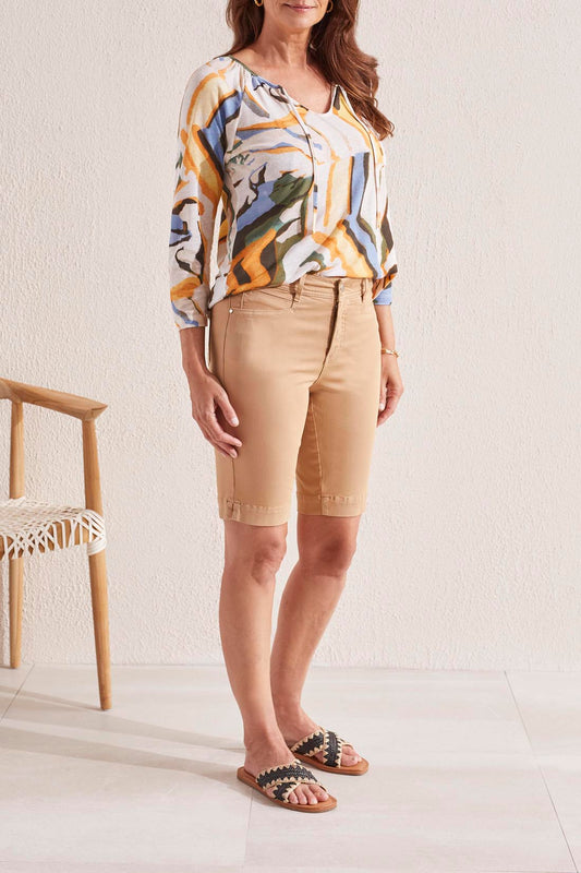 The back view of a woman wearing Tribal's Tan Front Fly Bermuda Short with Side Slits and a floral shirt.