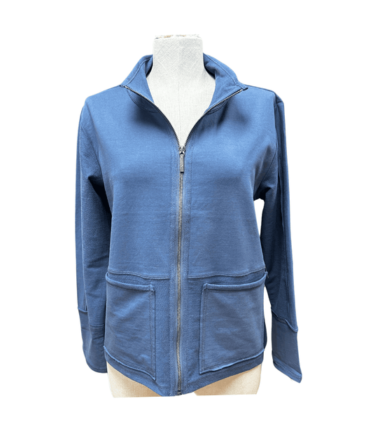 A woman stands against a white background in Escape’s Seaside knit jacket—a vibrant red layer over a white top, paired with floral wide-leg pants and sandals—ideal for transitioning through changing coastal weather.