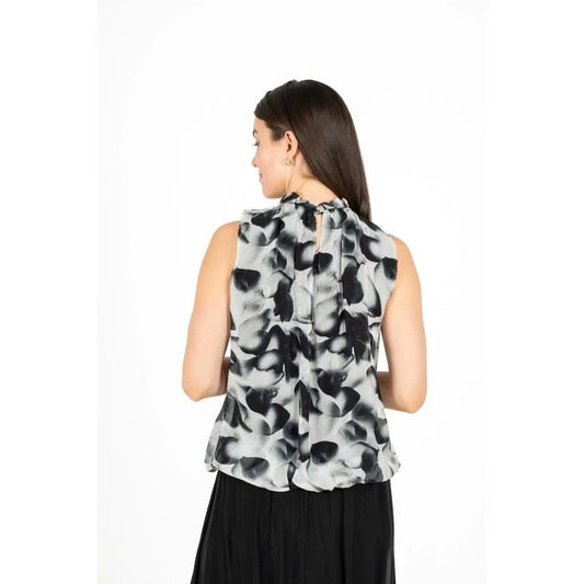 A woman is shown from the back wearing the Black Flowing Petals Blouse by M Made In Italy, featuring a sleeveless design and a high neckline with a black and white floral pattern.