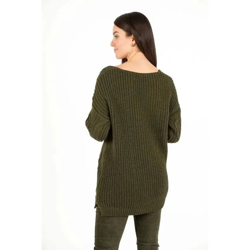 Dressed in an M Made In Italy Cable Knit Oversized V Neck Sweater paired with pants, a person stands with their arms crossed and a subtle smile against a plain white backdrop.