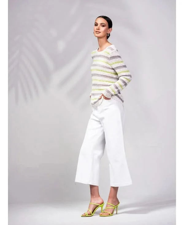 A person is wrapped in an Alison Sheri Striped Knit Sweater with green and white stripes, perfectly paired with white pants. The plain light gray background enhances the outfit's versatile and trendy appeal.