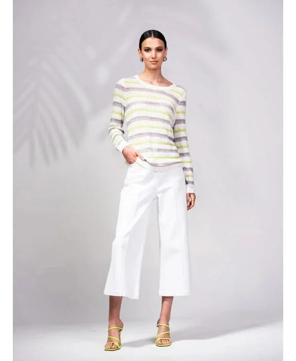 A person is wrapped in an Alison Sheri Striped Knit Sweater with green and white stripes, perfectly paired with white pants. The plain light gray background enhances the outfit's versatile and trendy appeal.
