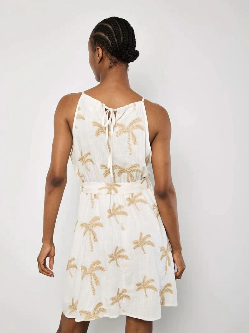 A woman in the Apricot Embroidered Palm Dress, featuring a breezy silhouette and beige palm embroidery, stands against a plain light background.