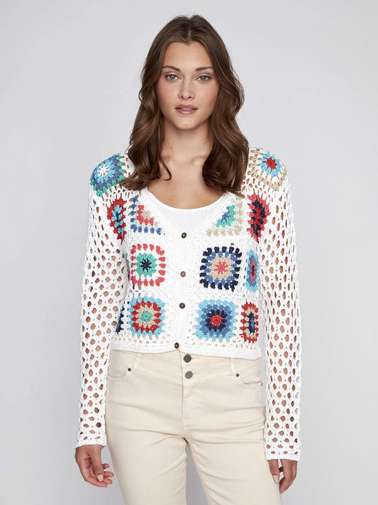 A woman models the CoCo Y Club Crochet Sweater—a cream cardigan with colorful squares—layered over a white top and beige pants, set against a plain light background.
