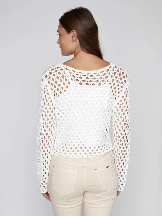 A woman models the CoCo Y Club Crochet Sweater—a cream cardigan with colorful squares—layered over a white top and beige pants, set against a plain light background.