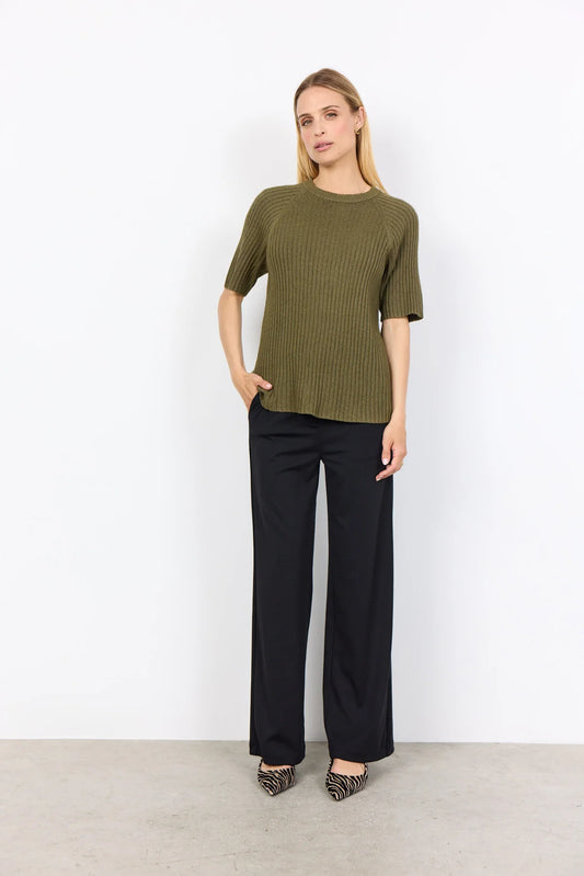 A person wearing the Soya Concepts Dark Olive Long Sleeved Knit in a relaxed fit with black pants stands against a plain white background, hands in pockets.
