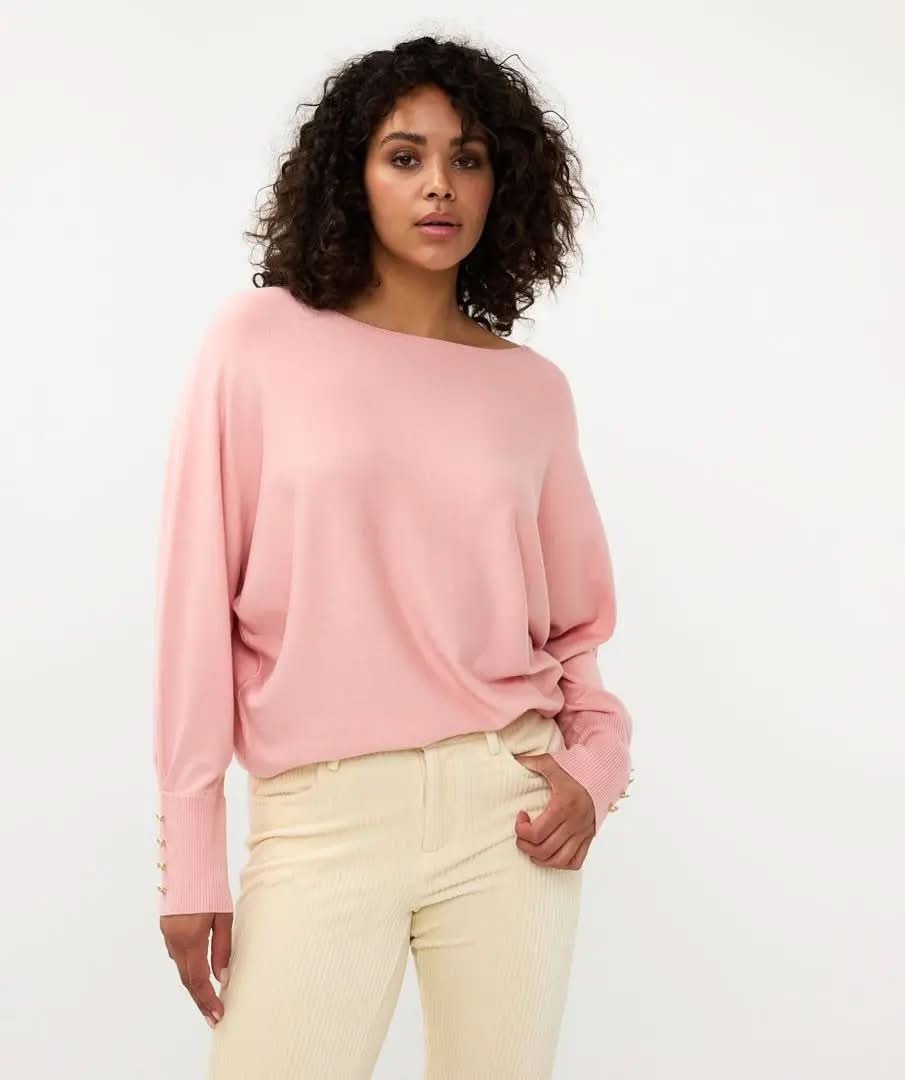 A person with curly hair is standing with their back to the camera, wearing Esqualo's pink Batwing Sweater with buttoned cuffs and light-colored pants.