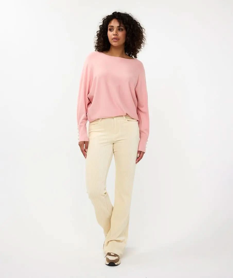 A person with curly hair is standing with their back to the camera, wearing Esqualo's pink Batwing Sweater with buttoned cuffs and light-colored pants.