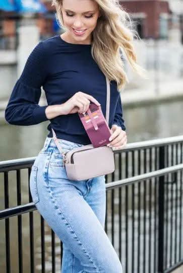 A woman sitting on a bench with a blue Kedzie Slim Zippered Wallet that has card slots.