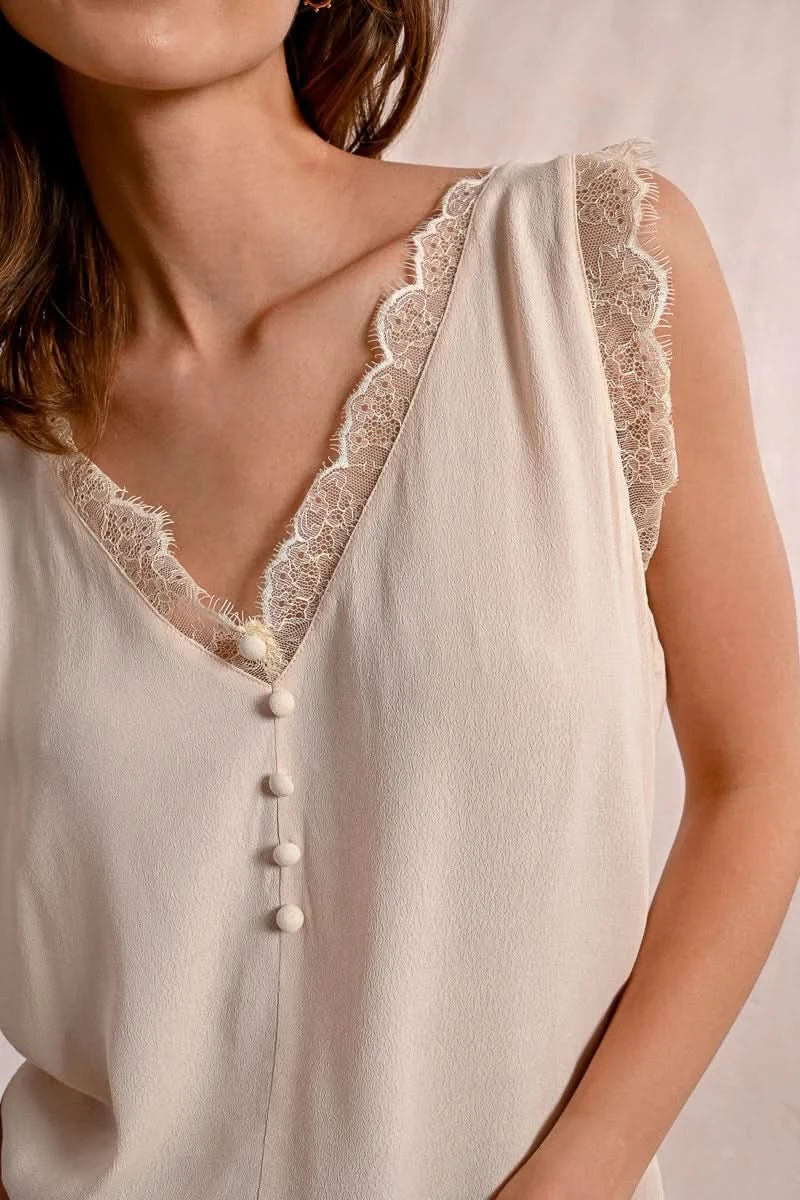 A woman embodies feminine elegance in Molly Bracken's Lace Camisole, a cream sleeveless top with delicate lace trim around the v-neckline and a row of small buttons down the front.
