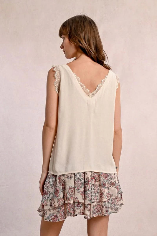A woman embodies feminine elegance in Molly Bracken's Lace Camisole, a cream sleeveless top with delicate lace trim around the v-neckline and a row of small buttons down the front.