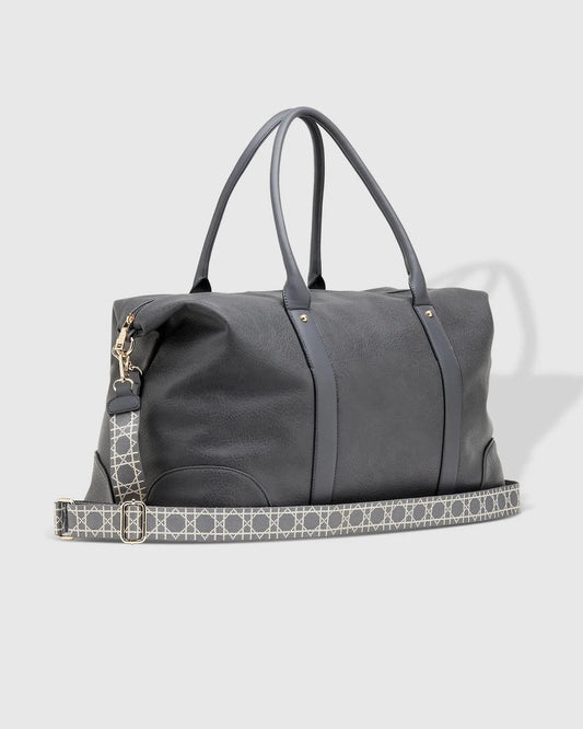 The Alexis Ezra Weekender Travel Bag by Louenhide is a large, dark gray bag made from vegan leather. It features two top handles and an adjustable, patterned shoulder strap.