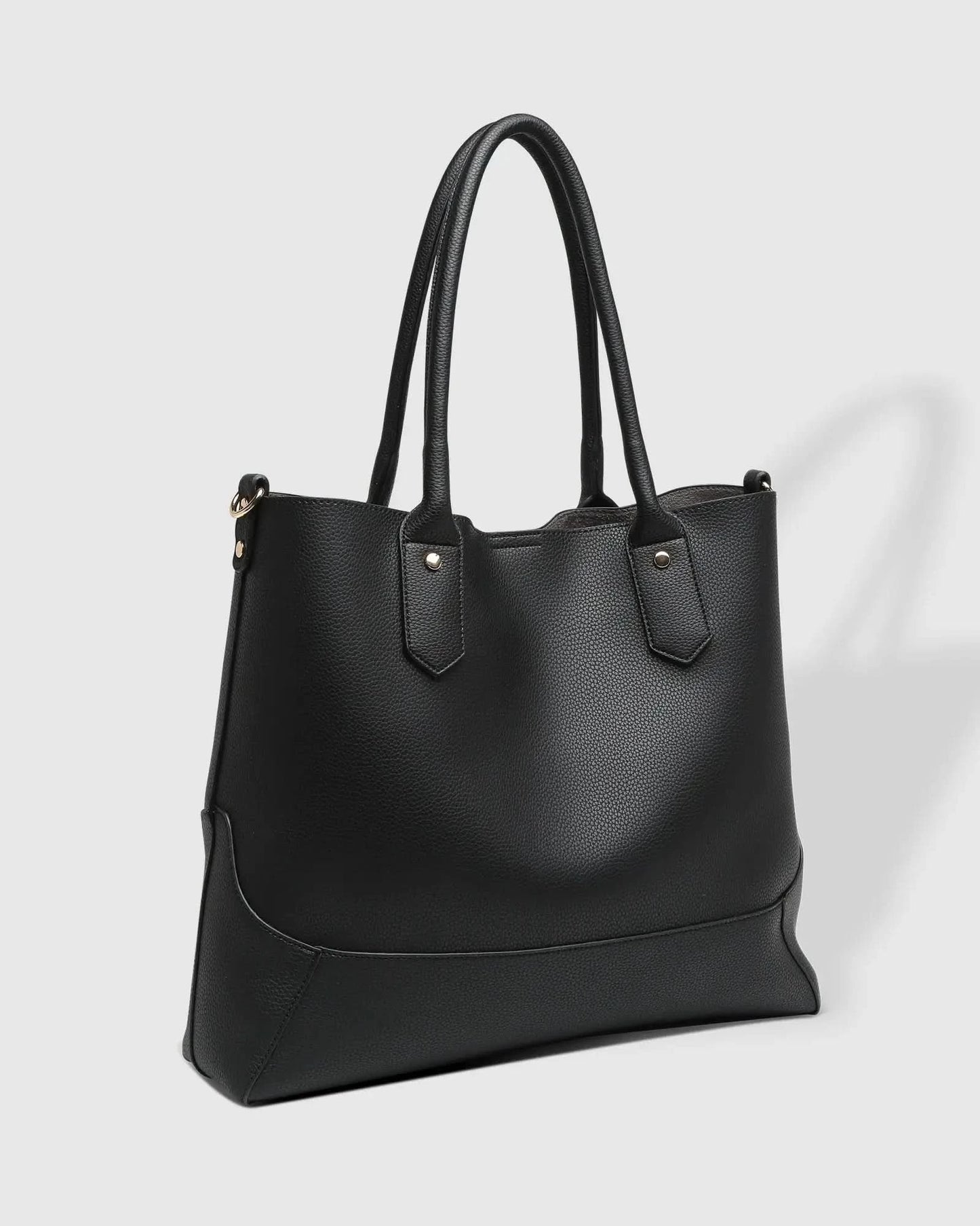 A person with blonde hair in a white outfit poses against a white wall, holding a large black Portsea Tote Bag from Louenhide made of vegan leather over their shoulder.