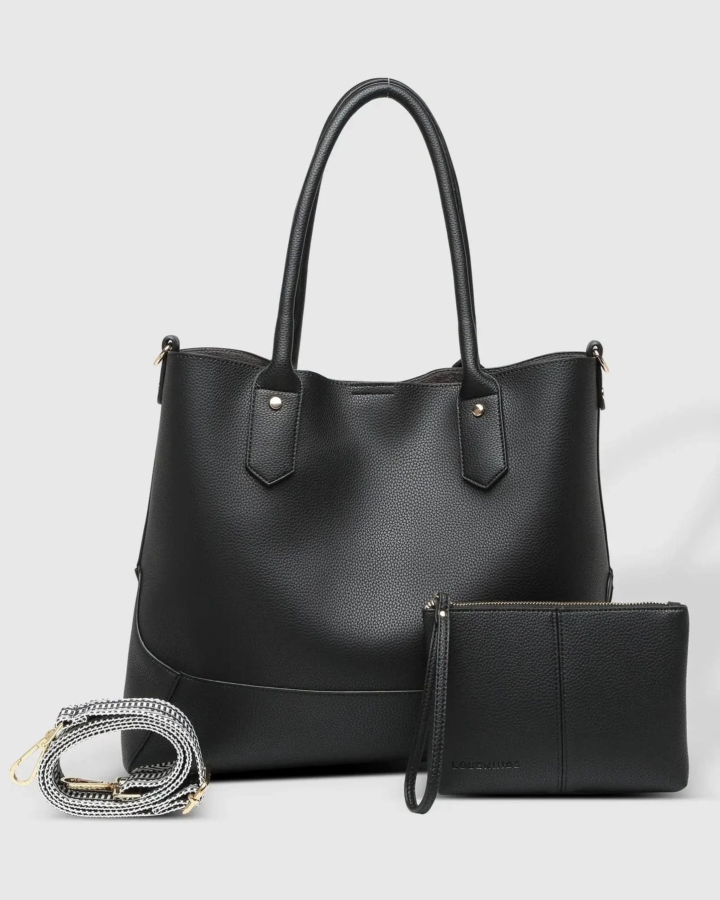 A person with blonde hair in a white outfit poses against a white wall, holding a large black Portsea Tote Bag from Louenhide made of vegan leather over their shoulder.
