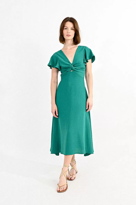 Woman posing in a stylish green Molly Bracken Long Cross-Bust Dress with capped sleeves and strappy sandals.