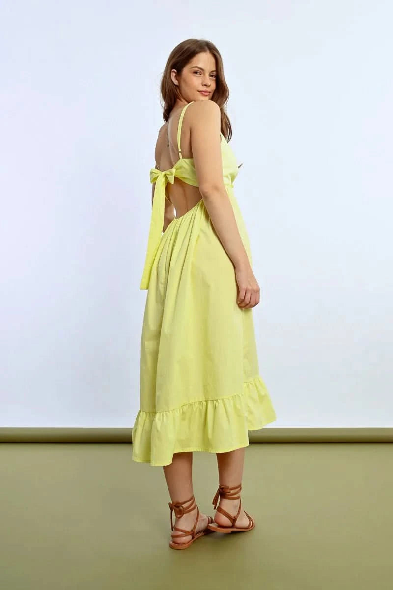 The person wears a Molly Bracken Ruffled Long Dress featuring a sleeveless design, crossed sweetheart neckline, and bow detail at the back, showing tattoos while posing sideways against a plain backdrop.