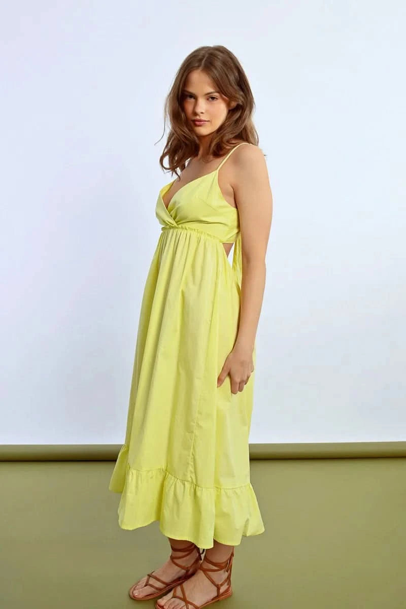 The person wears a Molly Bracken Ruffled Long Dress featuring a sleeveless design, crossed sweetheart neckline, and bow detail at the back, showing tattoos while posing sideways against a plain backdrop.