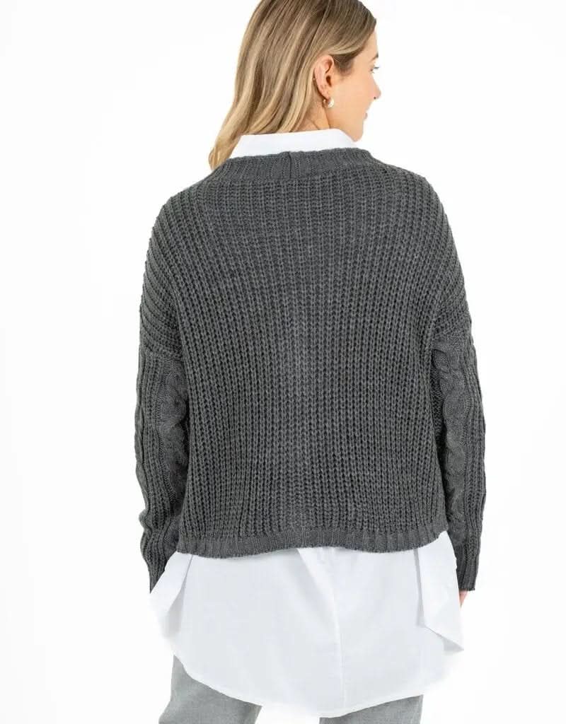 A person smiling, exuding comfort and style, is wearing a dark gray Knitted Cardigan by M Made In Italy over a white shirt and light gray pants, standing against a crisp white background.