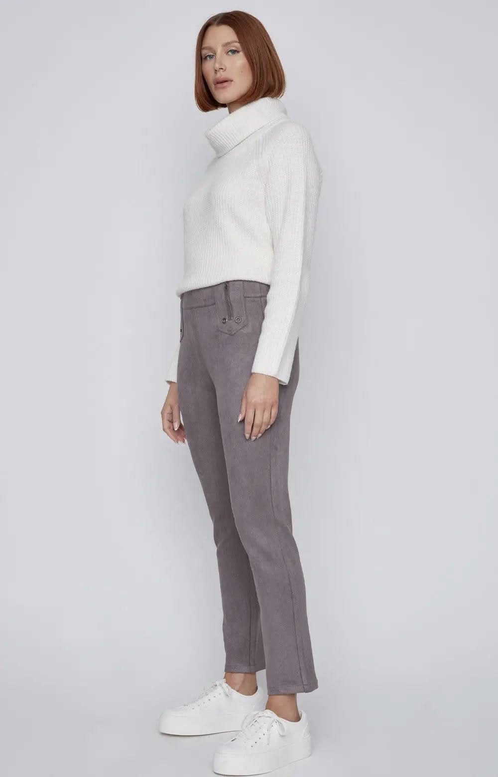 A person with short red hair is standing against a plain background, wearing a white turtleneck sweater, CoCo Y Club gray Front Zip Detail Pant, and white sneakers.