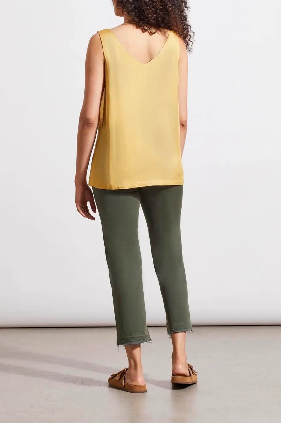 A woman in a Tribal Dijon Reversible V-Neck Cami and green jeans stands against a neutral background, accessorized with a gold necklace and brown sandals.