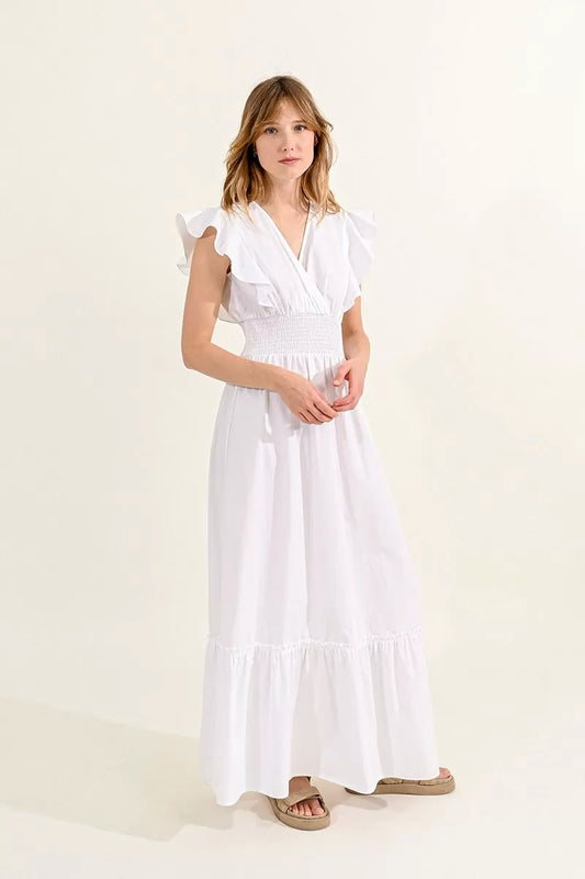 A woman in a white Molly Bracken ruffled V-neck maxi dress with a smocked waist standing against a neutral background.