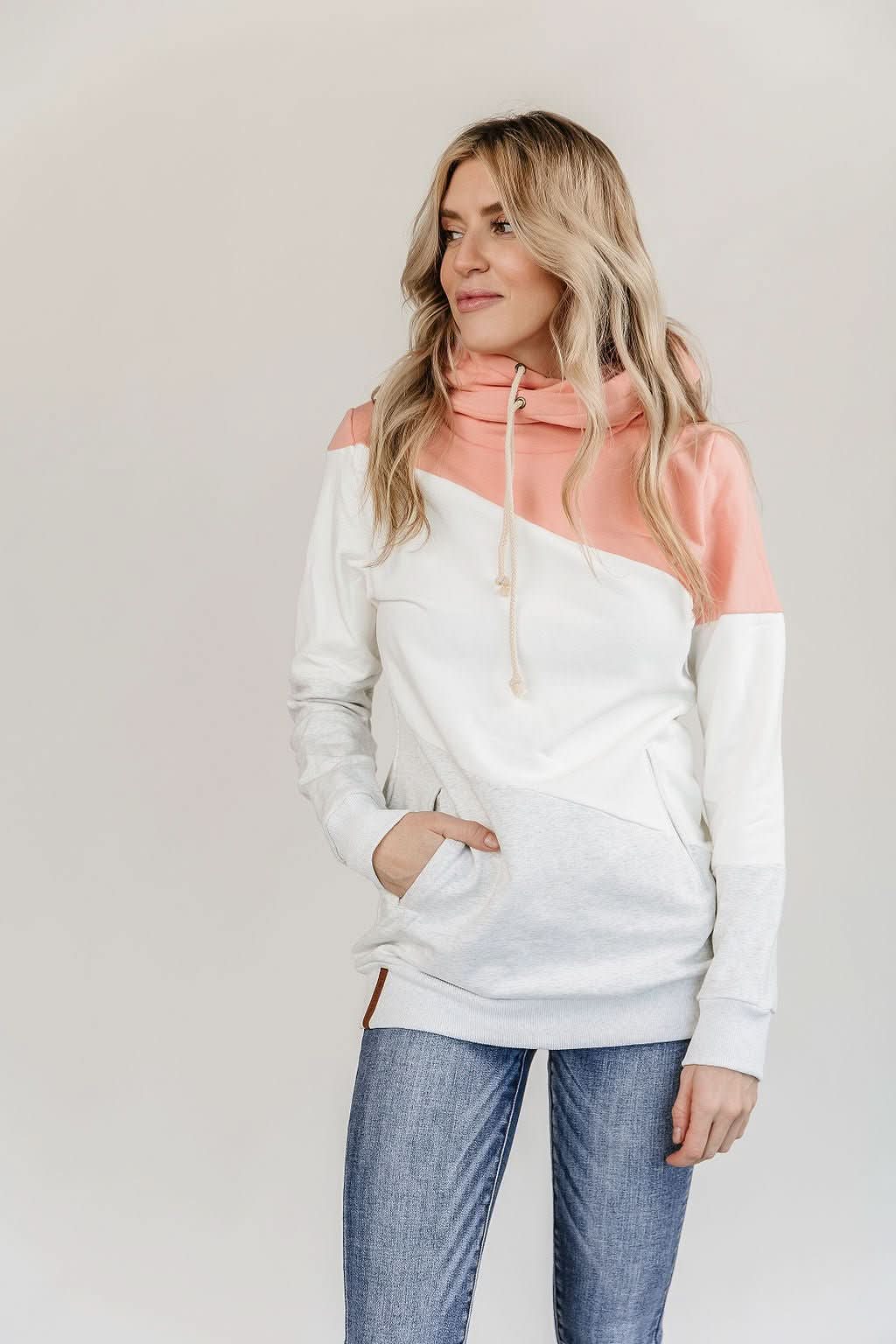 Clad in the cozy, color-blocked Be Fearless Singlehood Sweatshirt by Ampersand Avenue, featuring a harmonious blend of pink, white, and gray tones, a person stands confidently against a plain background. Paired with blue jeans, this sweatshirt effortlessly captures the essence of style and independence.