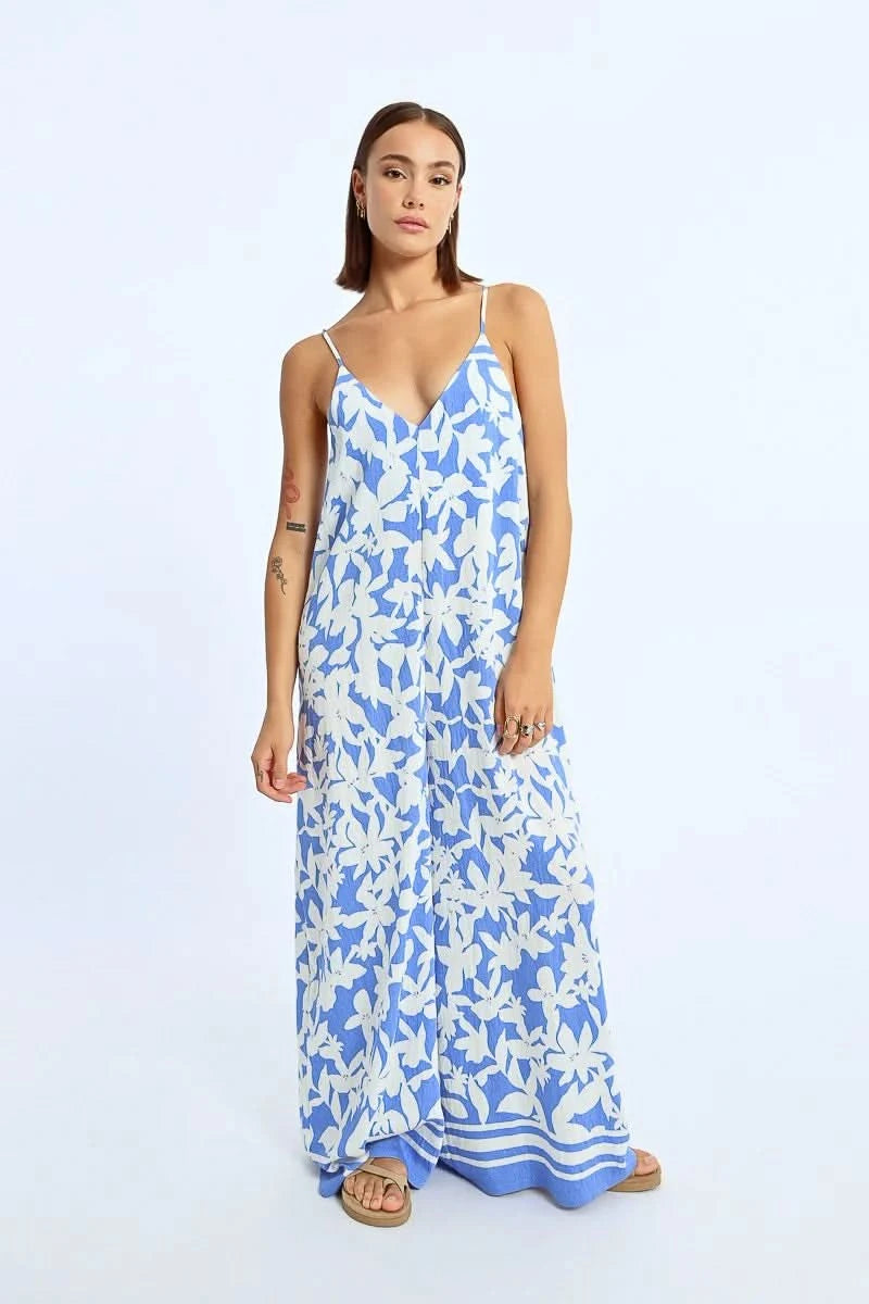 A woman exudes effortless style in a Molly Bracken Wide Leg Strappy Jumpsuit, paired with sandals, against a plain background.