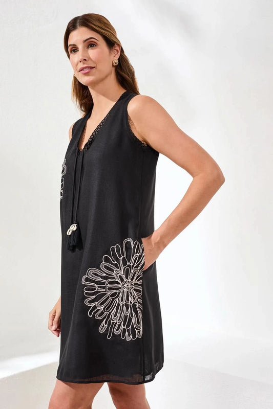 A woman stands indoors by a potted plant, wearing the Tribal Embroidered V-Neck Sleeveless Dress, paired with tan heeled sandals and gold earrings.