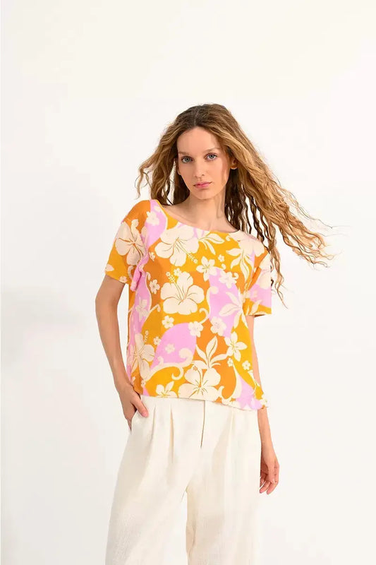 Woman in a floral orange Molly Bracken twisted back top and white pants posing against a neutral background.