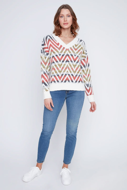 A woman in a CoCo Y Club V neck knitted Sweater with a multicolored zigzag pattern stands with one arm crossed, the other touching her chin, and pairs the cozy piece with blue jeans.