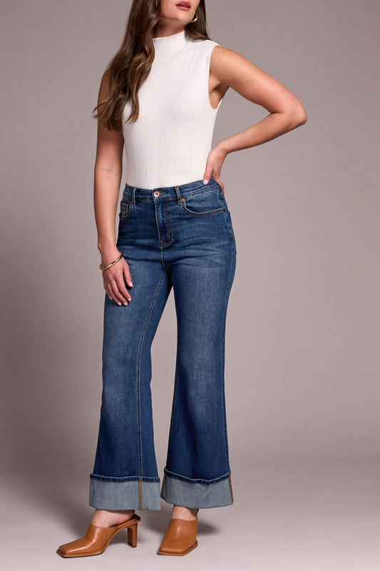 A woman stands with one hand in her pocket, wearing a sleeveless white turtleneck, Tribal BROOKE PALAZZO JEANS in antique blue, and tan heeled shoes.