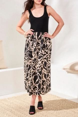 A woman wears the Tribal SLEEVELESS TWOFER DRESS, featuring a black top and an A-line beige and black abstract cotton skirt, styled with black open-toe heeled shoes.