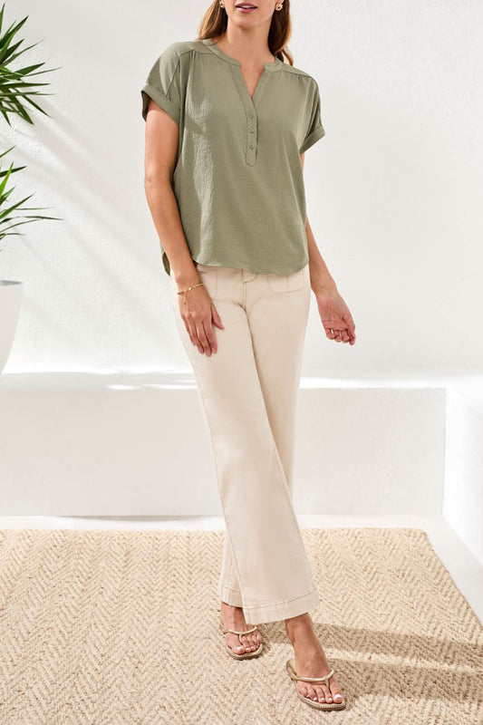 A woman stands indoors wearing a Tribal Pop Over Blouse with short sleeves in olive green, paired with cream-colored pants and sandals.
