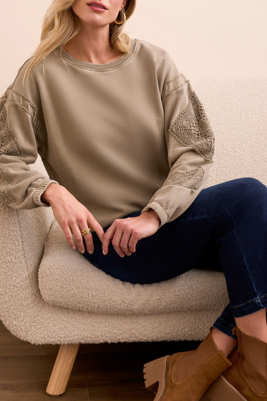 A woman stands indoors wearing the Tribal CREW NECK APPLIQUE DTL sweater, blue cropped jeans, and brown suede ankle boots, with a cream sofa in the background.