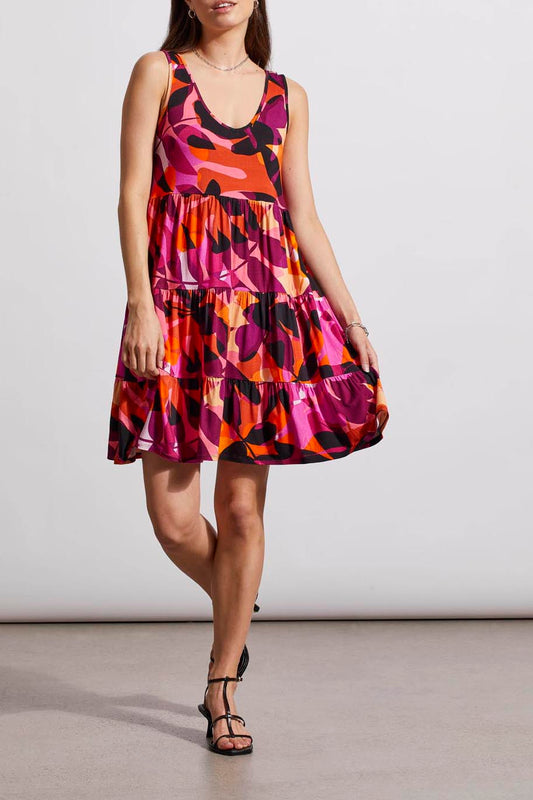 Woman wearing a bright and colourful sleeveless Tribal Short Tiered Knit Dress with abstract print, paired with black sandals, standing against a neutral background.