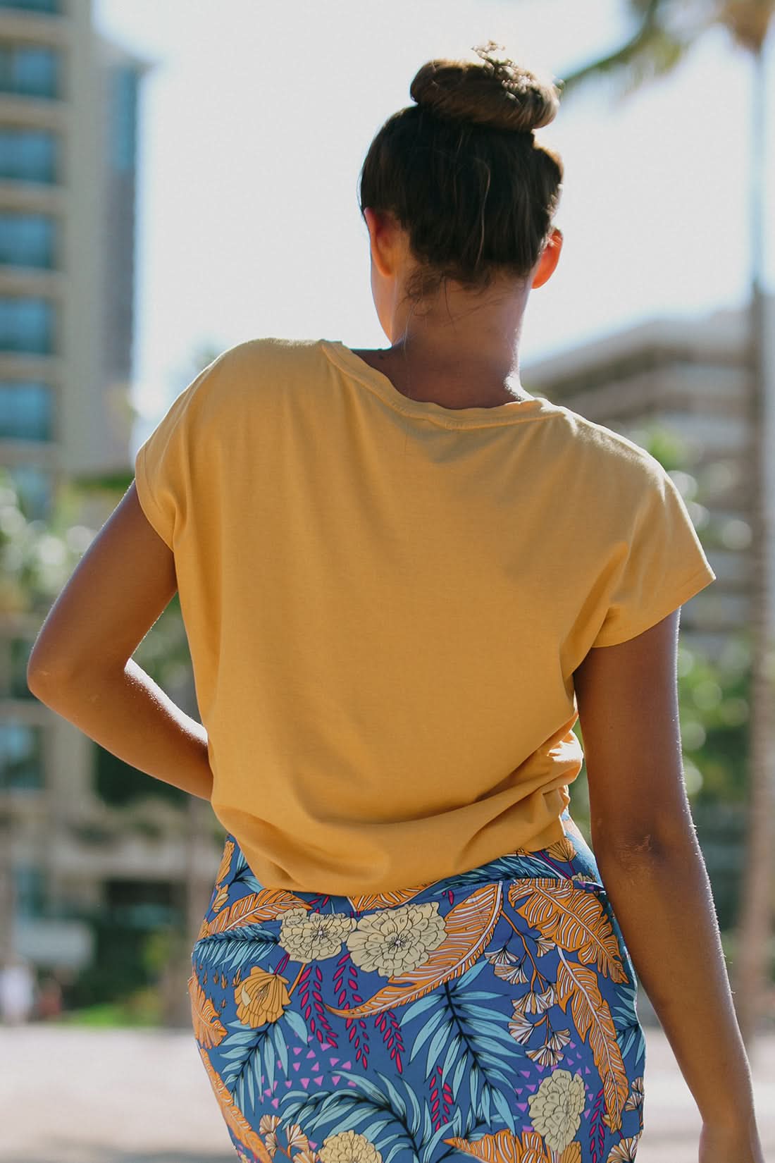 A woman stands outdoors in the Tribal CAP SLEEVE CREW NECK TOP and a blue floral skirt, with palm trees and a building behind her—a stylish choice for your next vacation wardrobe.