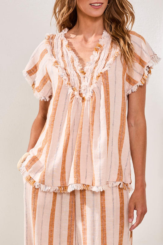 A woman with shoulder-length dark hair stands outdoors, smiling at the camera under a blue sky while wearing the Tribal Cap Sleeve T-Blouse.