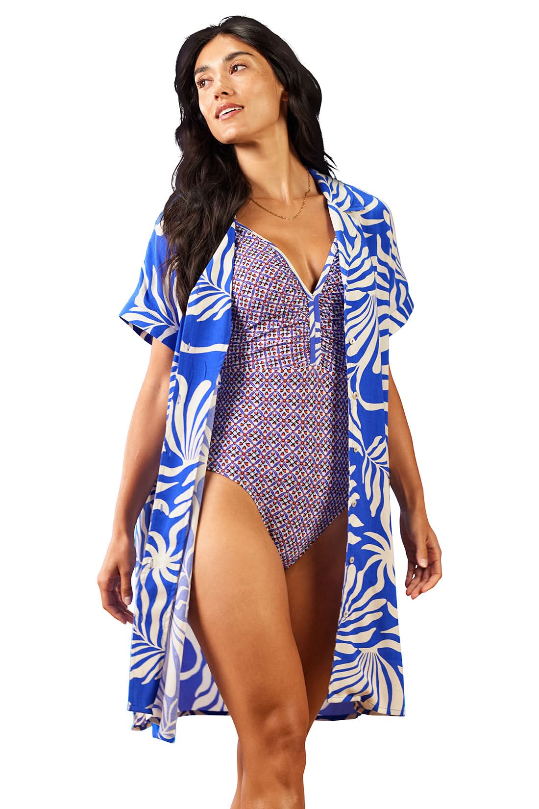 A woman stands looking to the side, wearing a patterned one-piece swimsuit and the Tribal Shirt Dress Cover Up With Back Rushing in blue and white floral Ecovero rayon.